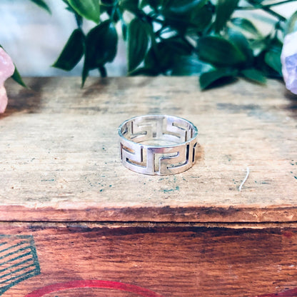 Alt text: Vintage sterling silver cut-out band ring with simple, minimal design on weathered wooden surface with floral arrangement in background