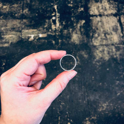 Vintage sterling silver cut out band ring held between fingers against rustic wooden background