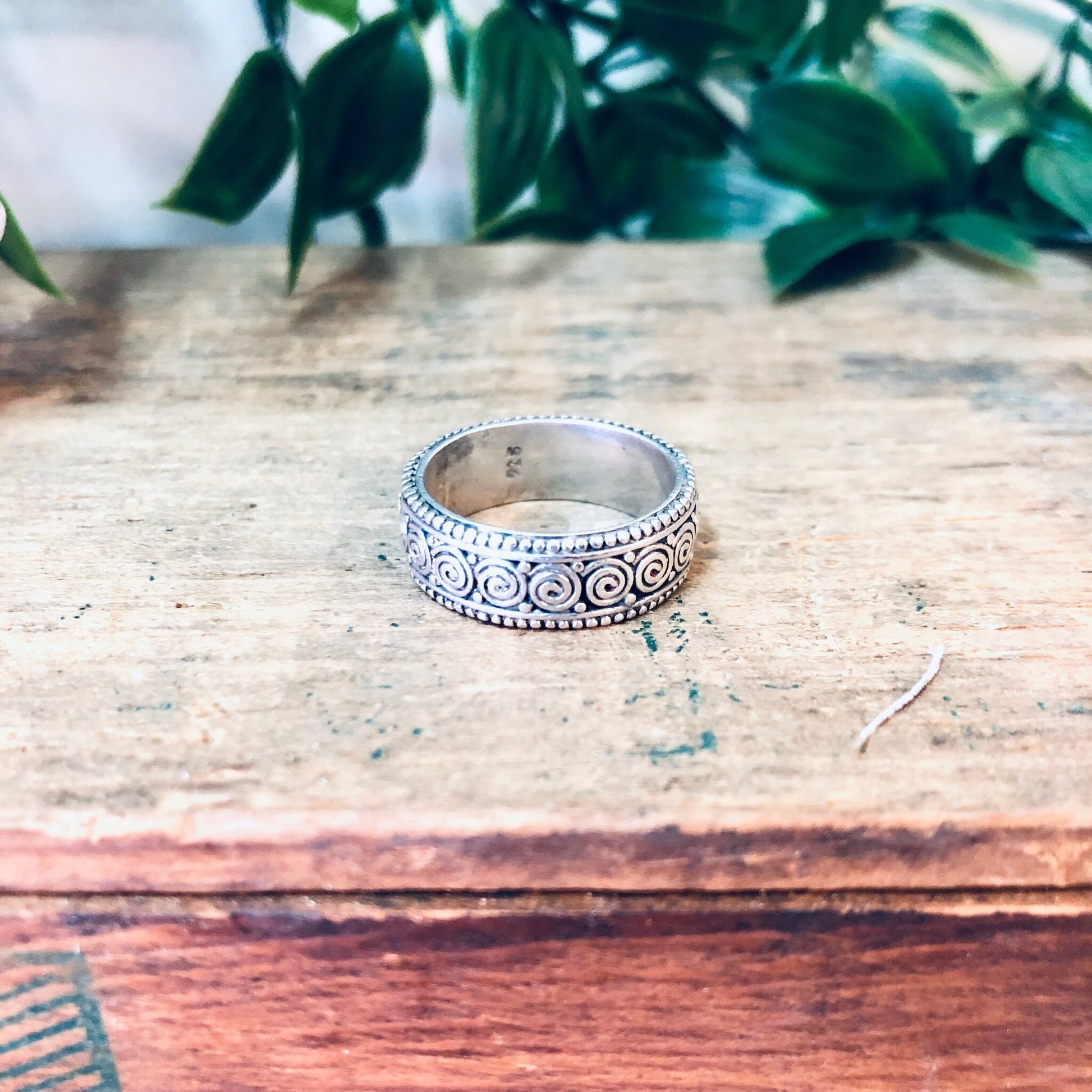 Vintage silver swirl design band ring on rustic wooden surface with green foliage in background