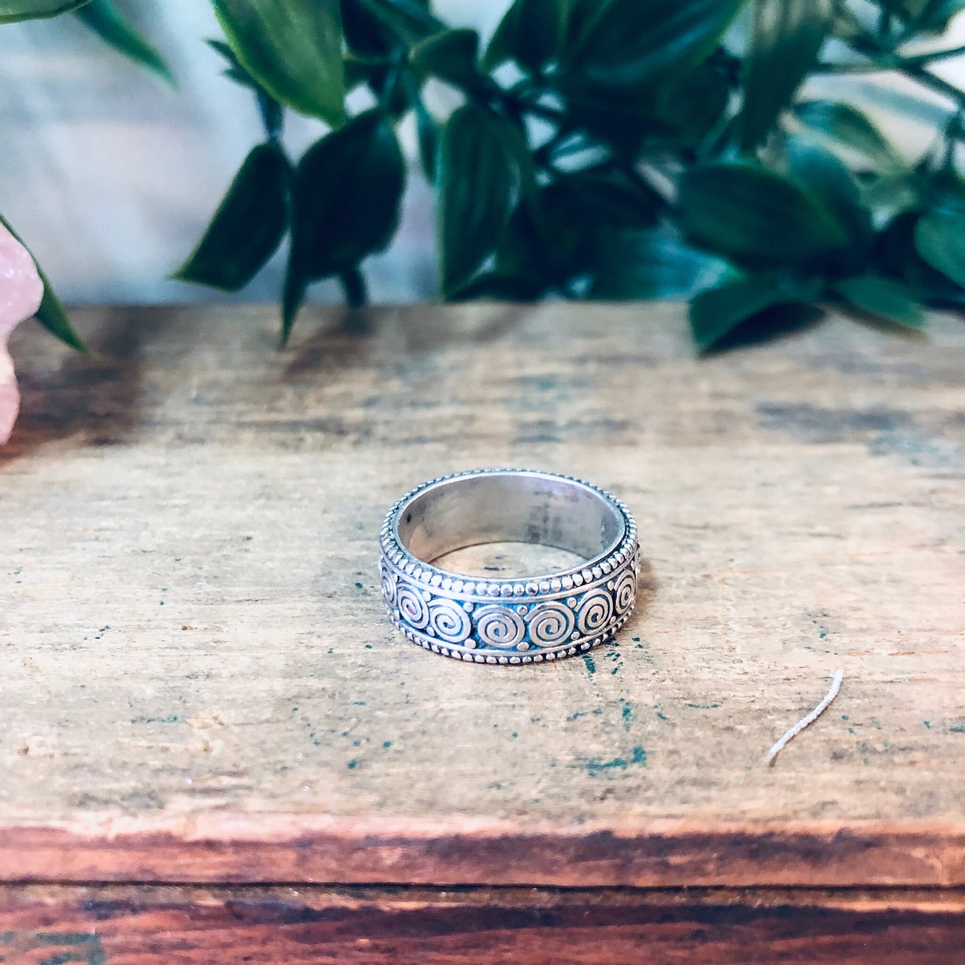 Vintage sterling silver swirl design band ring on weathered wooden surface with plant in background