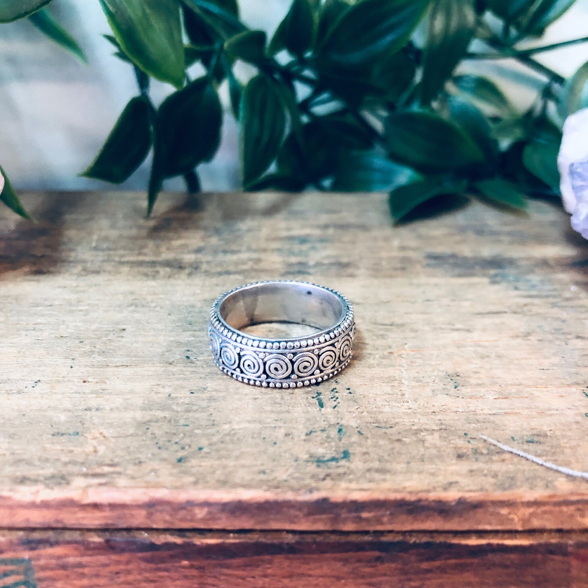 Vintage sterling silver swirl design band ring on weathered wooden surface with greenery in background