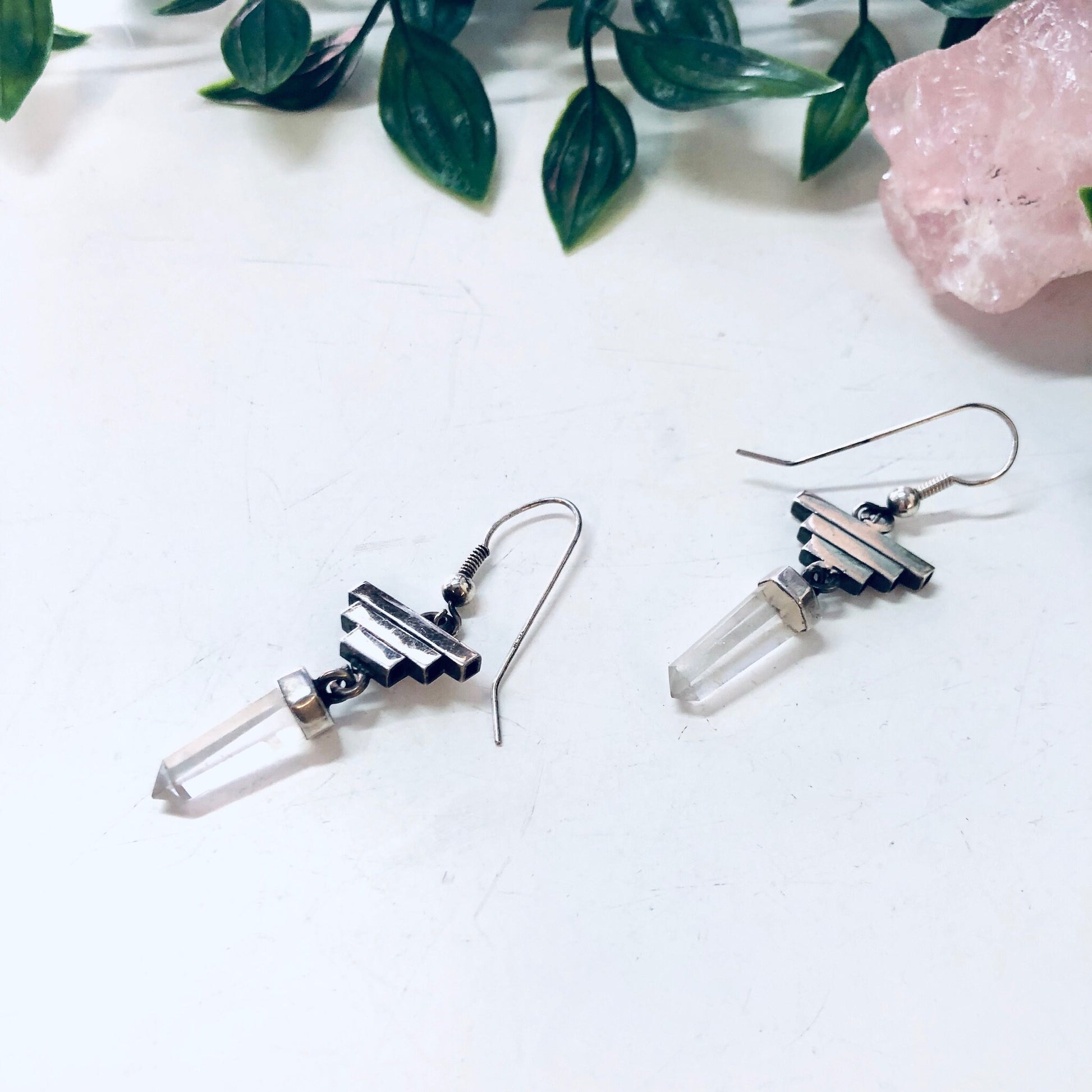 Vintage silver pyramid earrings with clear quartz crystal points on white background with green leaves and rose quartz crystal.