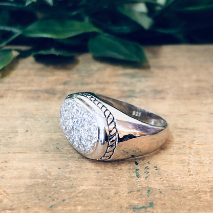 Vintage silver ring with faux diamond and rope design on rustic wood surface with green leaves in background