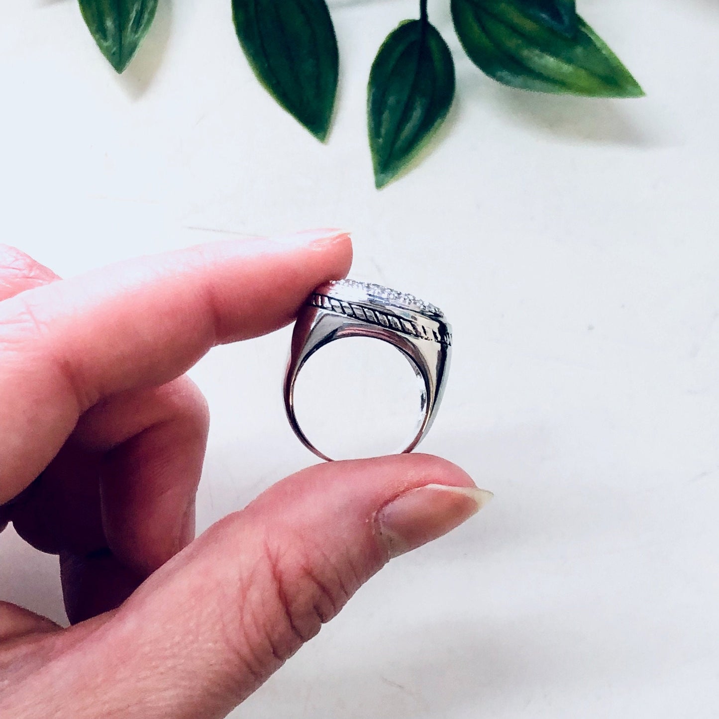 Vintage silver ring with rope design and faux diamond, held in front of green leaves on white background