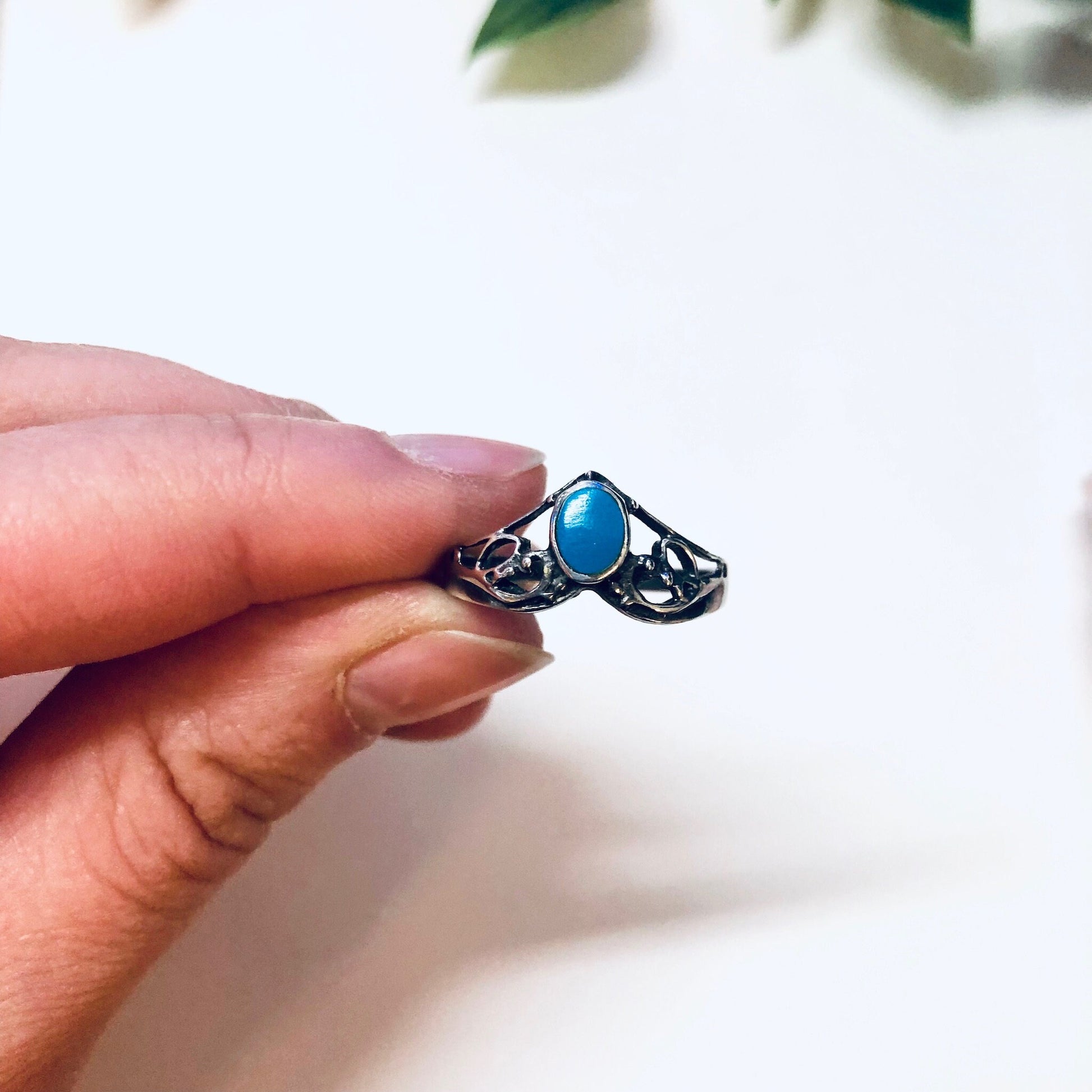 Vintage silver turquoise ring held between fingers, featuring a V-shaped design with an oval blue turquoise stone set in an intricate silver band, perfect for stacking and bohemian style.