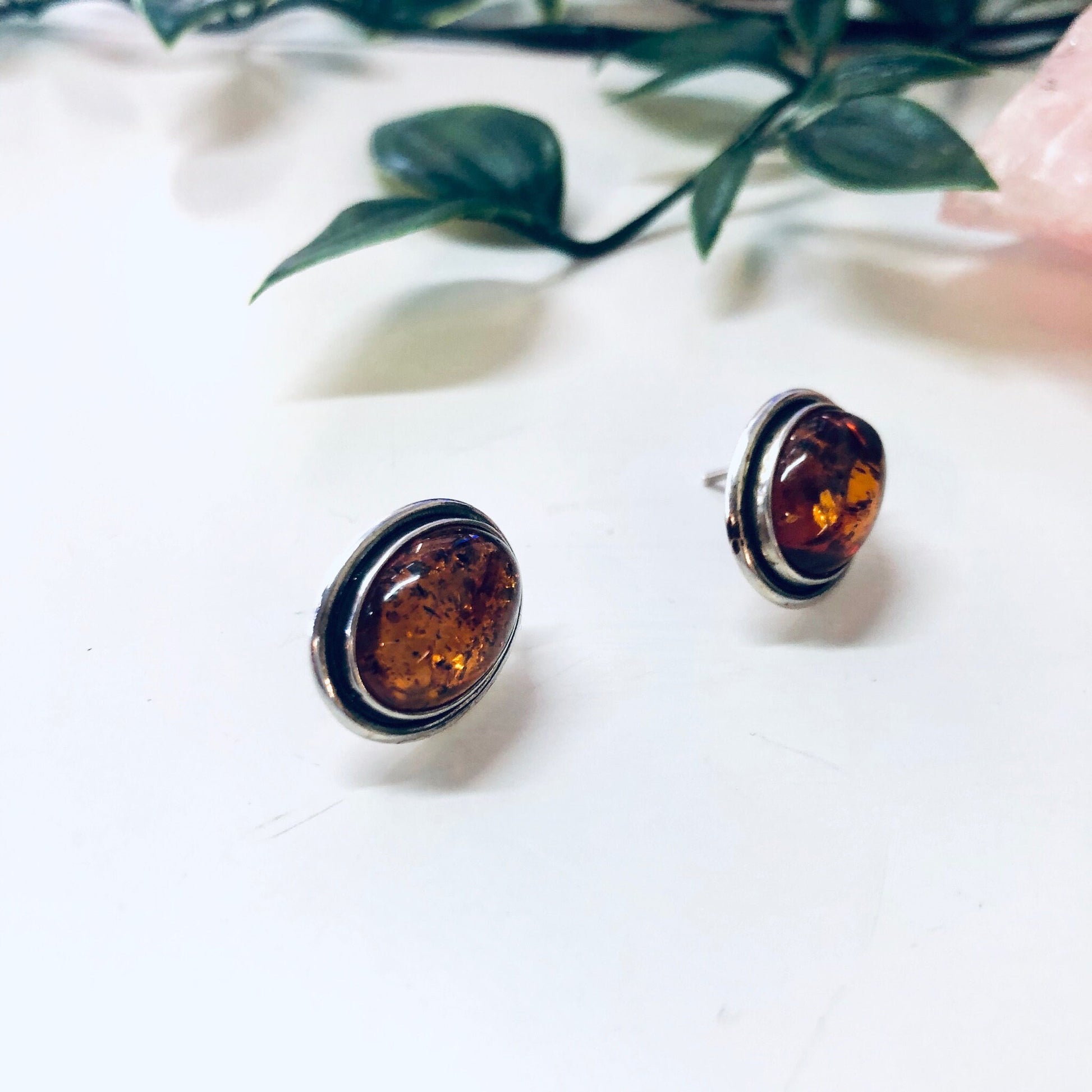 Vintage silver and amber stud earrings resting on white fabric with greenery in background