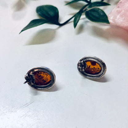 Vintage silver and amber stud earrings showcased with green leaves on a white background.