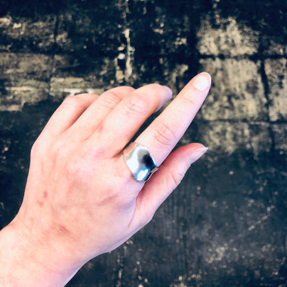 Vintage silver abstract minimalist ring on finger against dark textured background