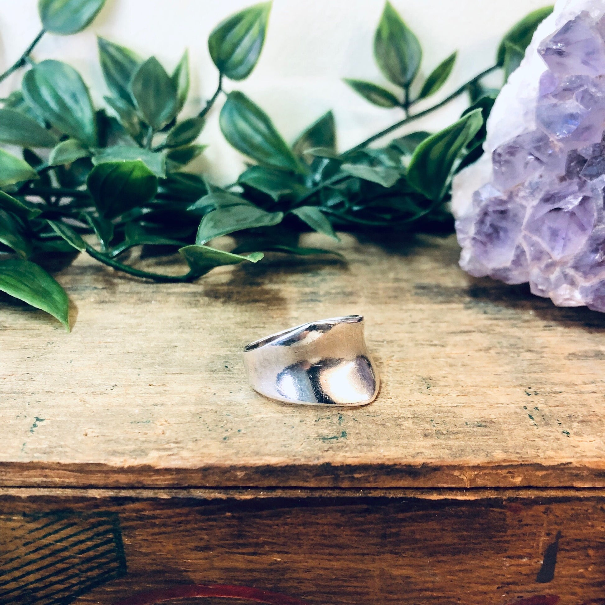 Vintage silver wrap ring on rustic wooden surface with amethyst crystal and lush green foliage in soft focus background