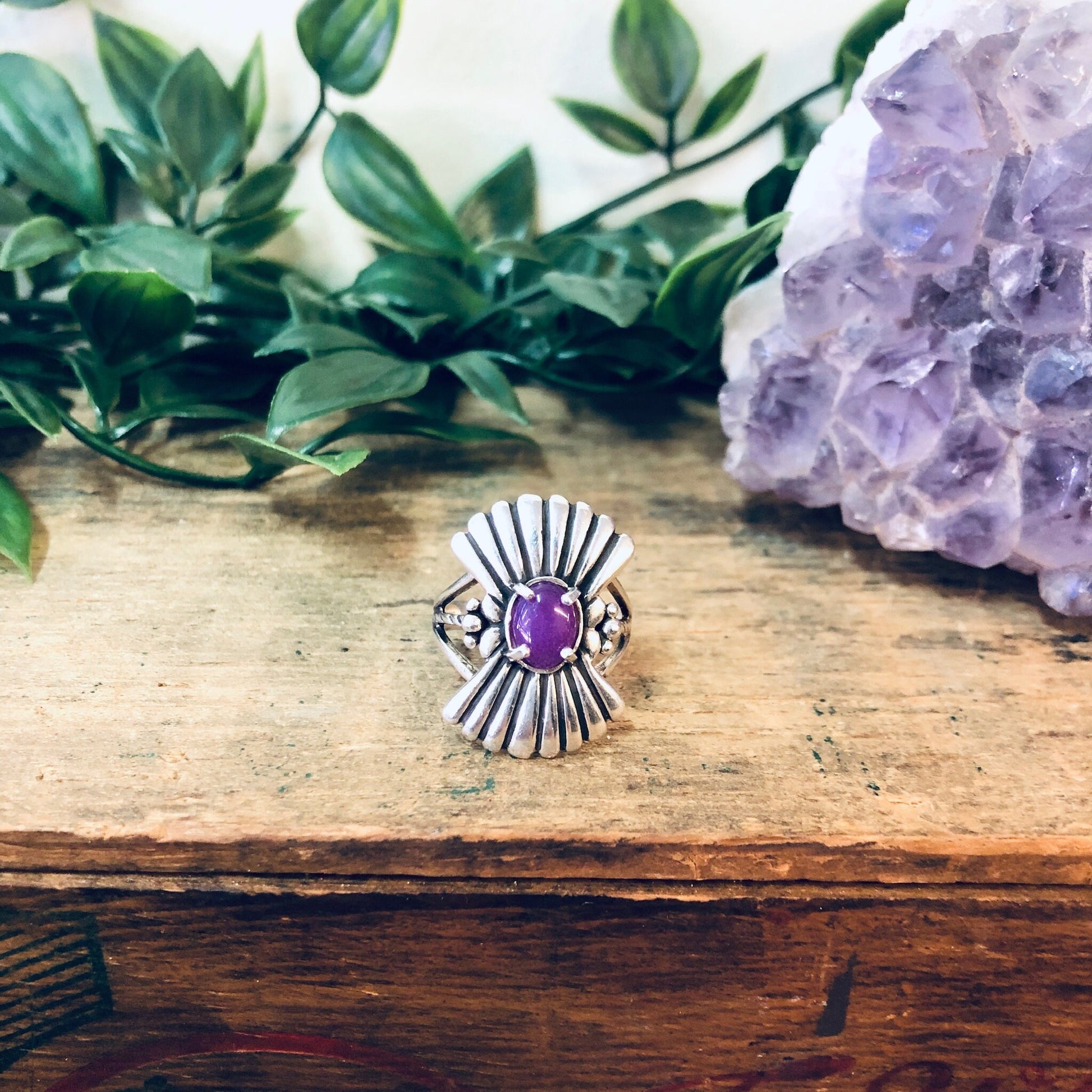 Vintage silver fan design ring with purple gemstone on wooden surface with greenery and pink amethyst geode crystal in background, unique boho statement jewelry