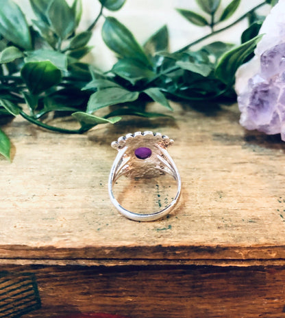 Vintage silver ring with unique pink and purple gemstone design on wooden surface with greenery in background