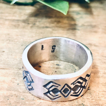 Vintage silver band ring with geometric tribal design on wooden surface with leaves.