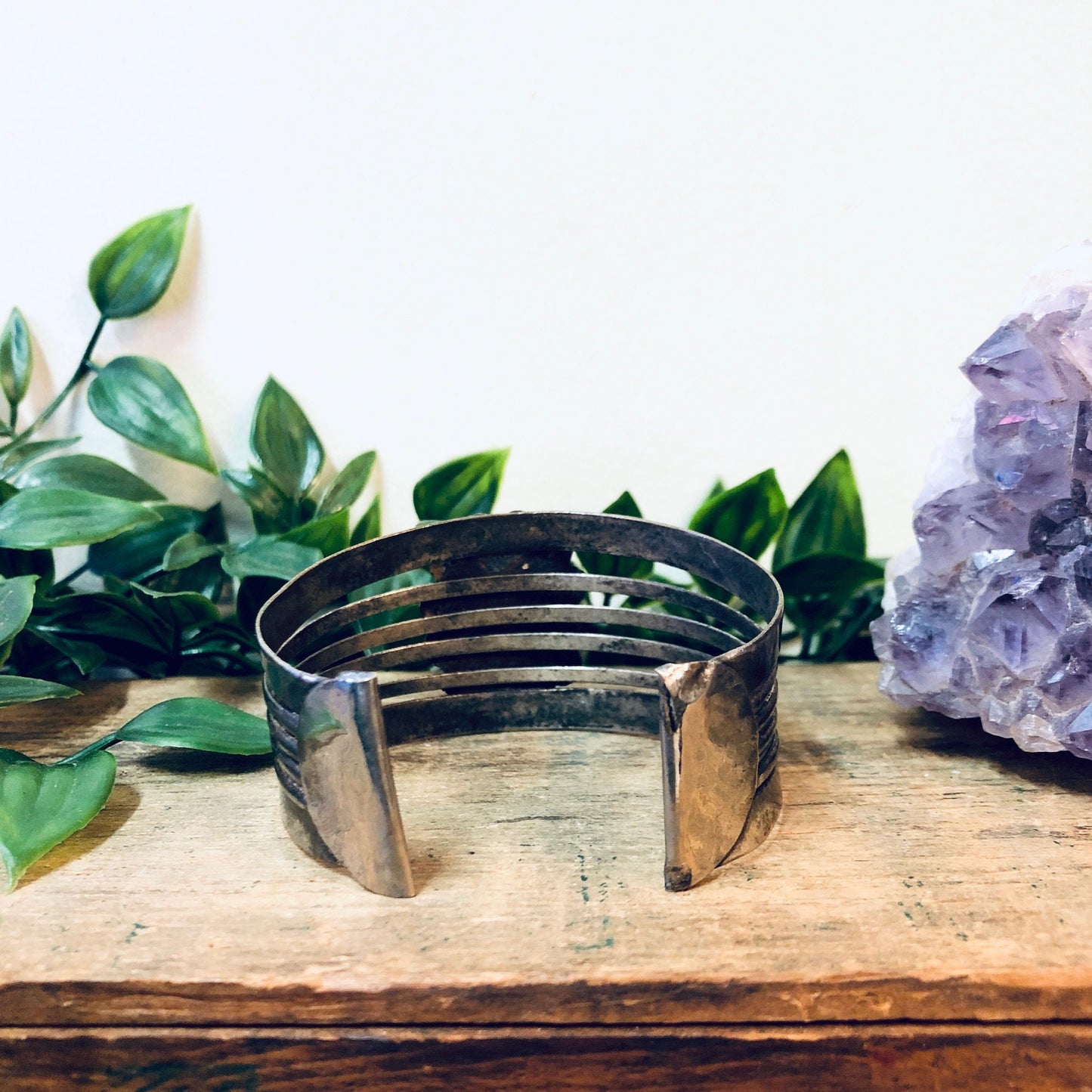 Vintage silver-toned cuff bracelet with blue scarab design, displayed on wooden surface with leaves and amethyst crystal.