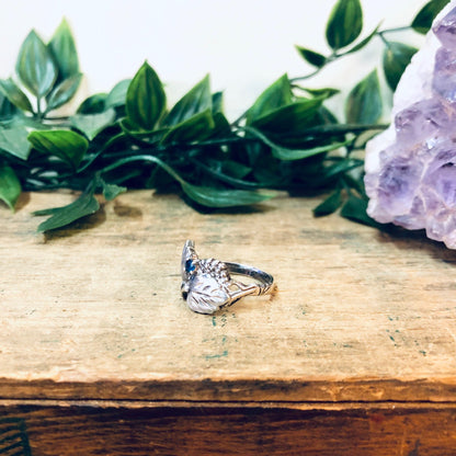 Vintage silver leaf ring with blue gemstone on wooden surface near amethyst crystal and green leaves