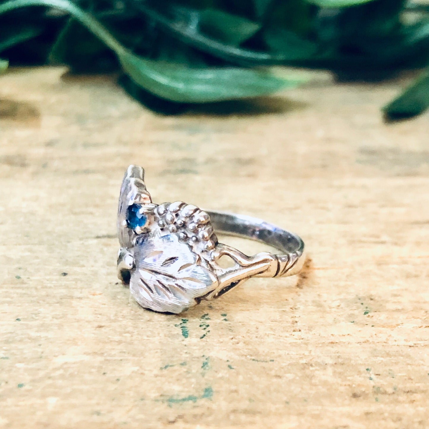 Vintage silver leaf ring with blue gemstone on rustic wooden surface, perfect anniversary or birthstone gift