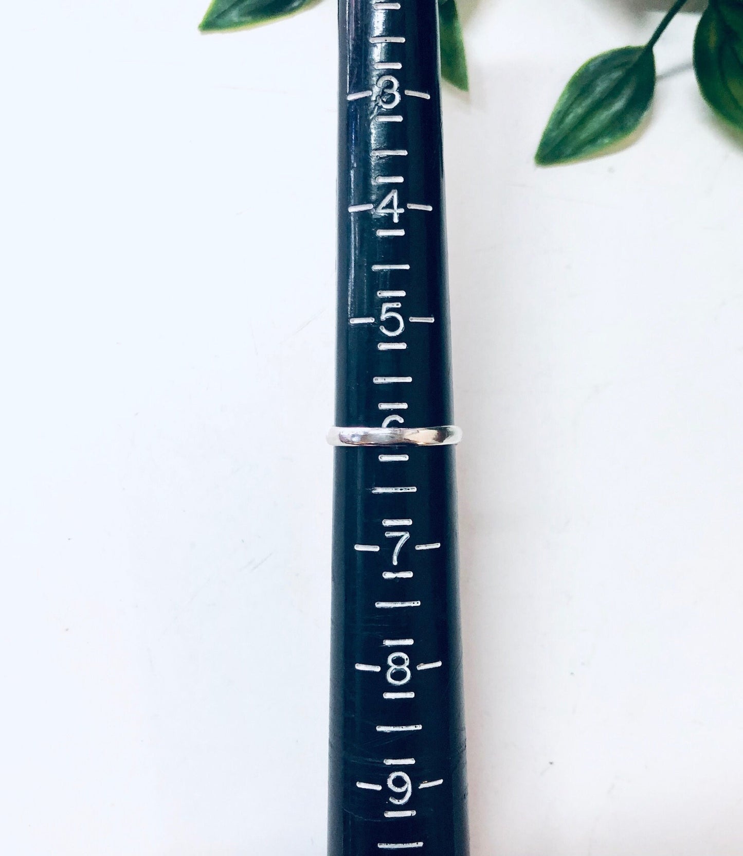 Vintage navy blue enamel and silver ring with measurement markings, placed next to green leaves on a white background.