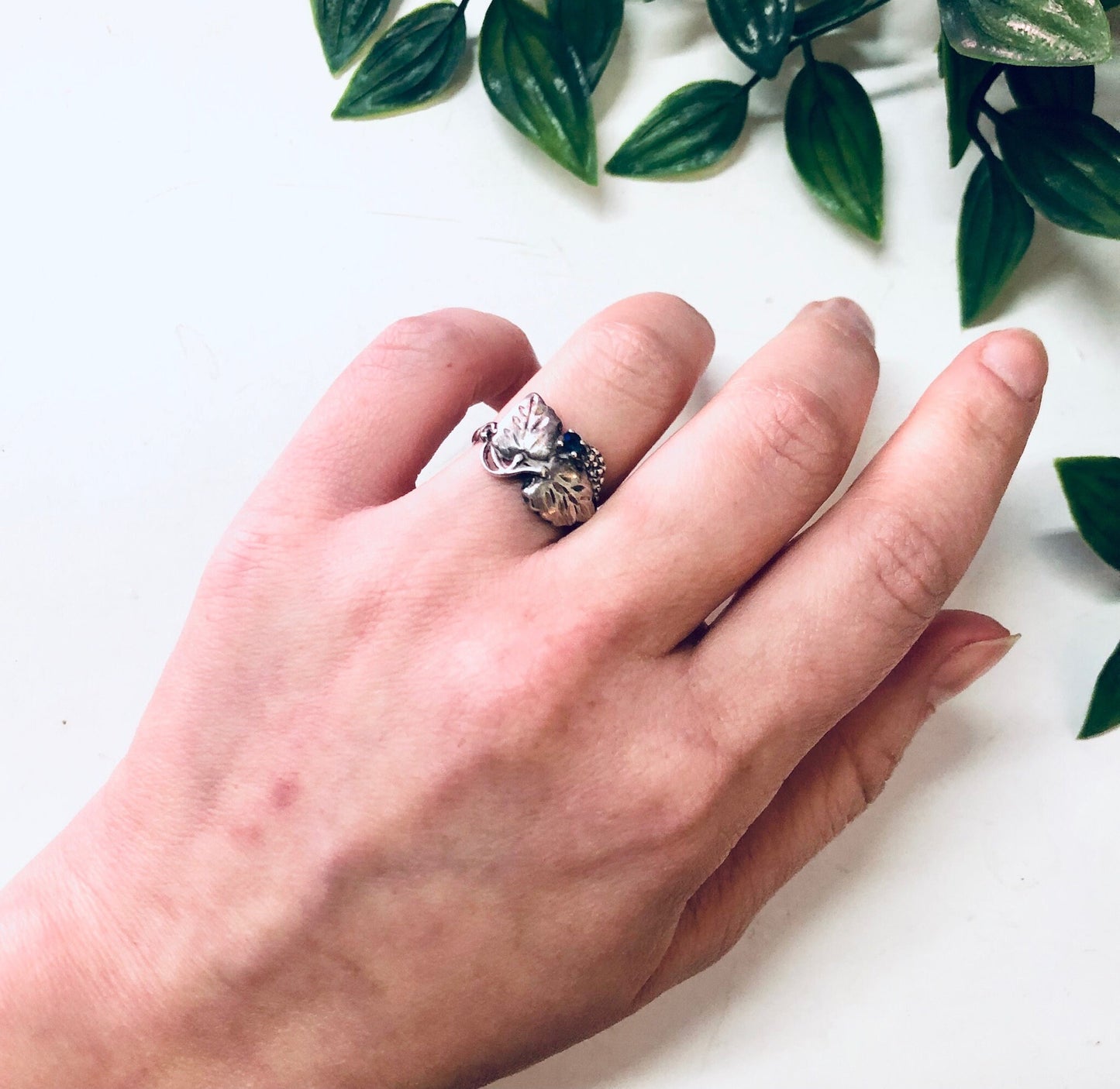 Vintage silver leaf ring with blue gemstone on hand against white background with greenery