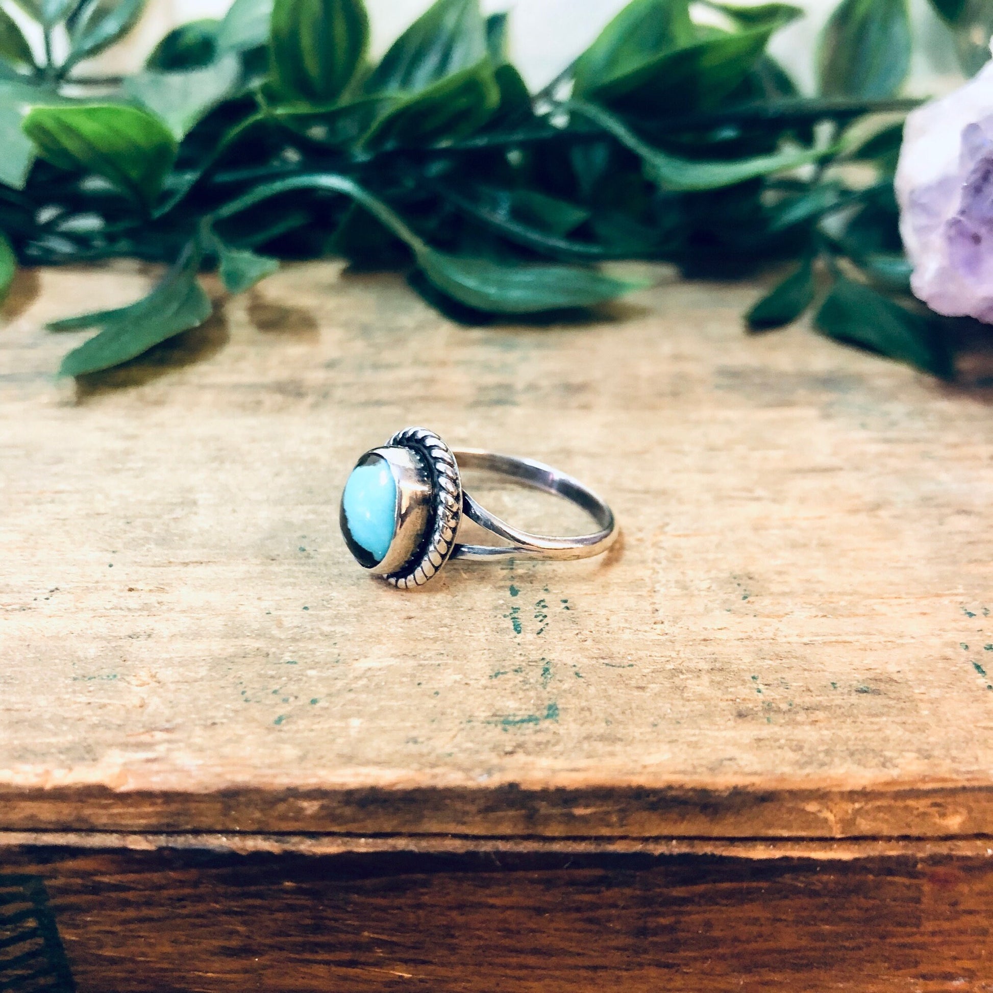 Vintage silver ring with blue and brown cabochon stones on wooden surface with green plant leaves in background