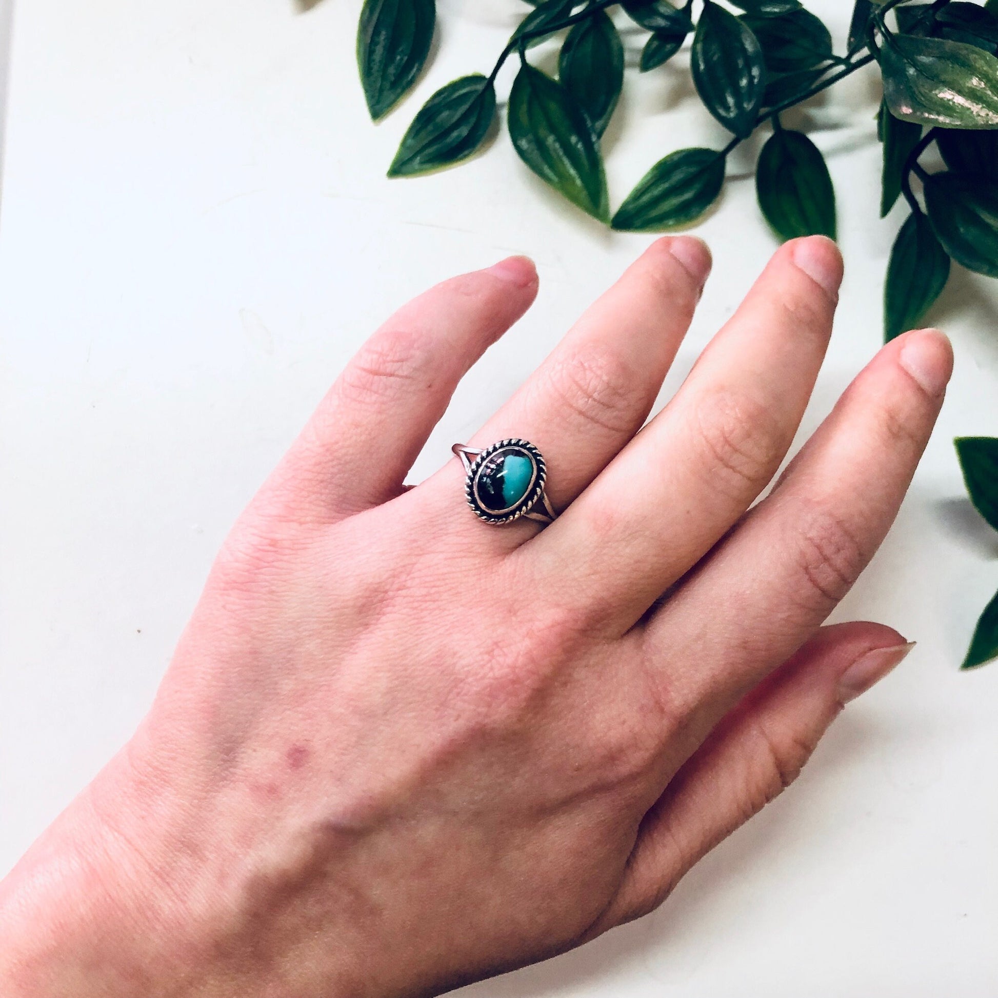 Vintage silver ring with blue cabochon stone on a hand against a white background with green leaves