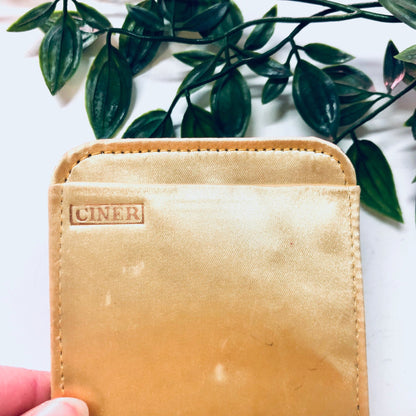 Vintage gold-toned Ciner compact and lipstick tube held in front of green foliage