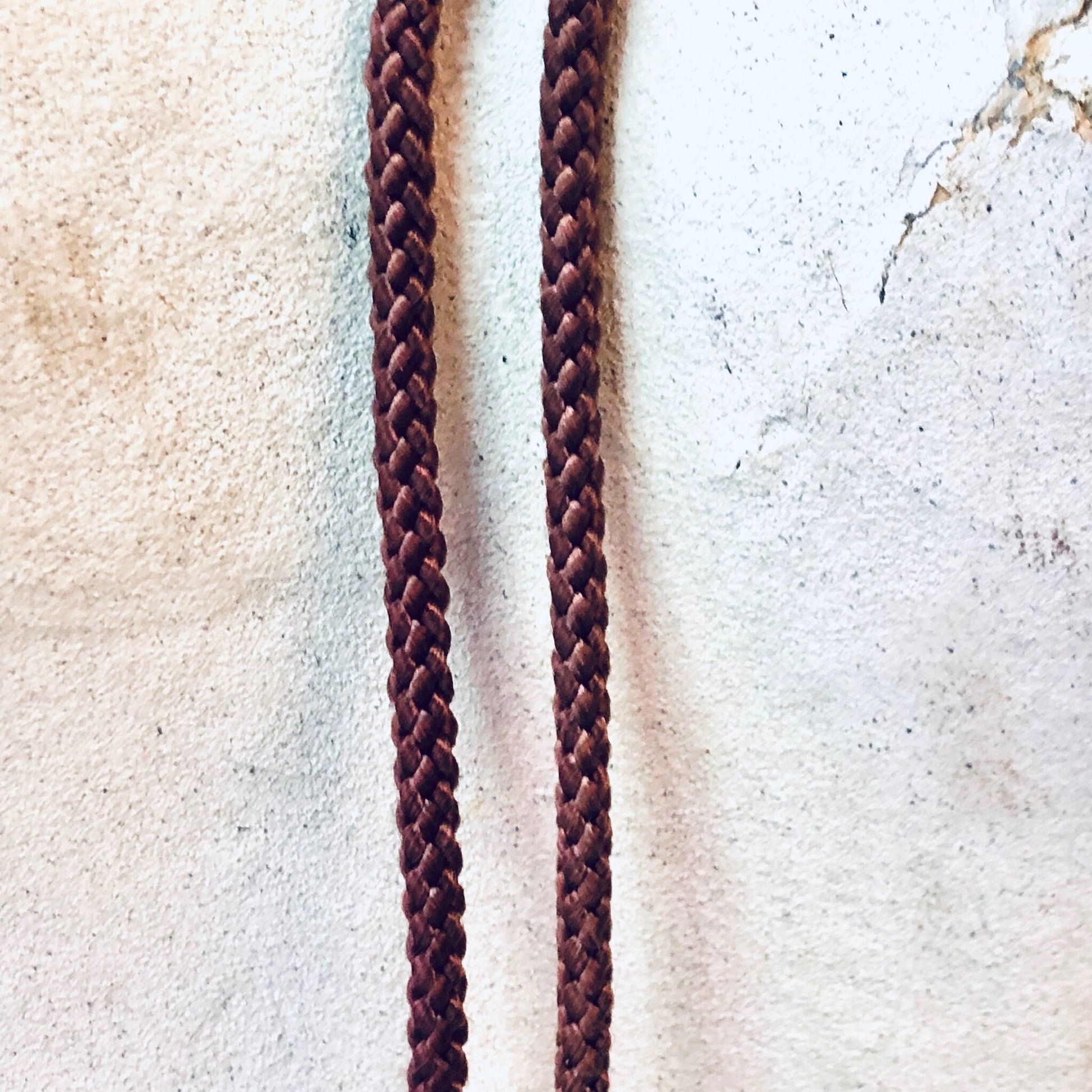 Braided brown leather cords with intricate knot pattern on textured beige background, vintage Japanese bolo tie or rope tie design, close-up detail view