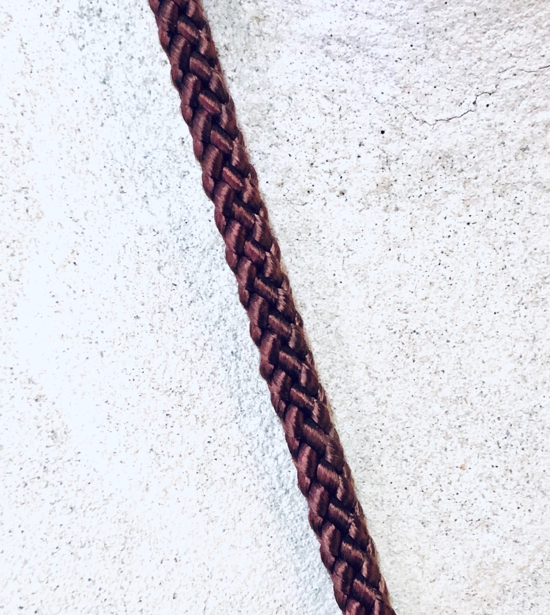 Braided brown and burgundy rope on white textured background, creating a vertical line down the center of the image.