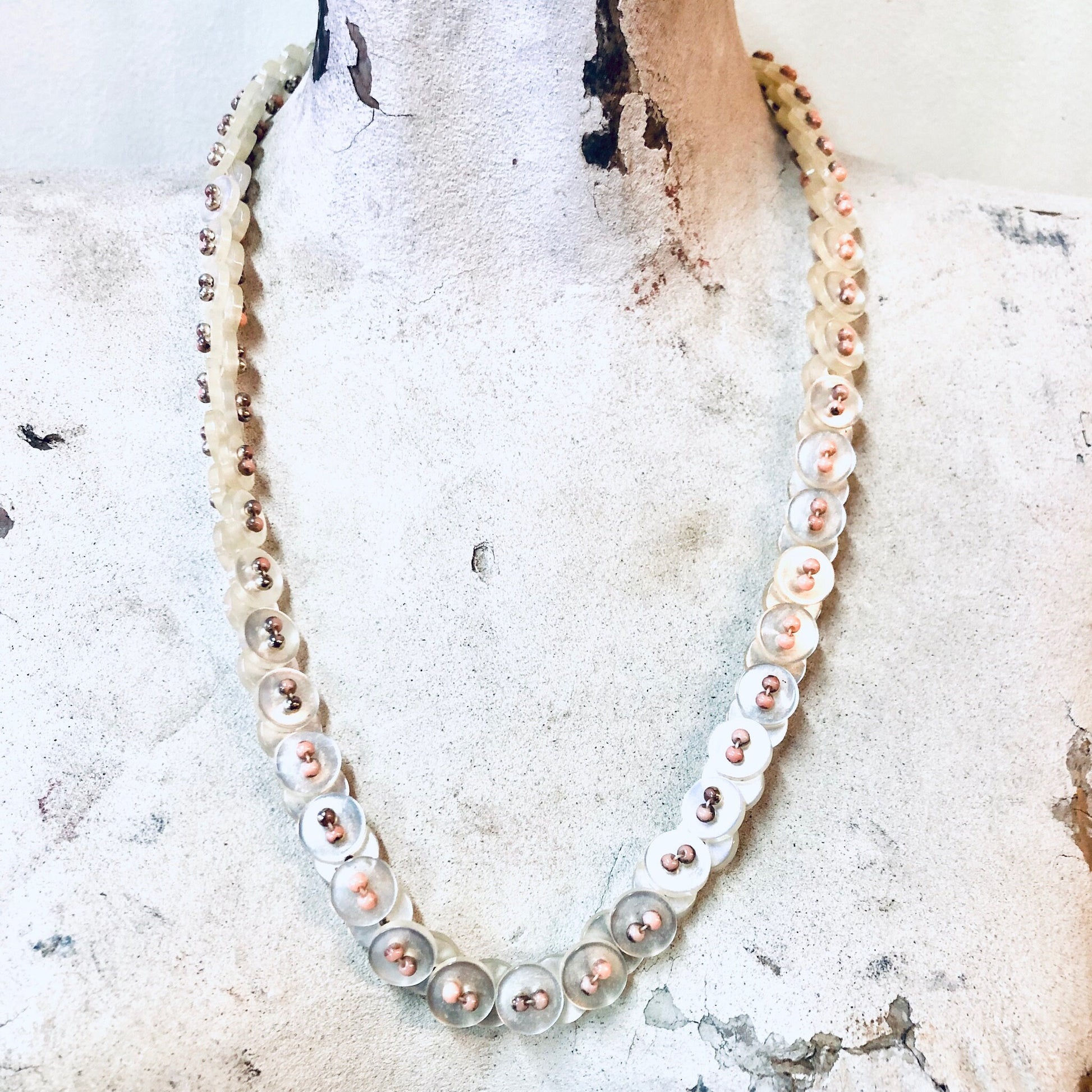 Vintage pearlescent button necklace with white and pink beads on weathered wood surface