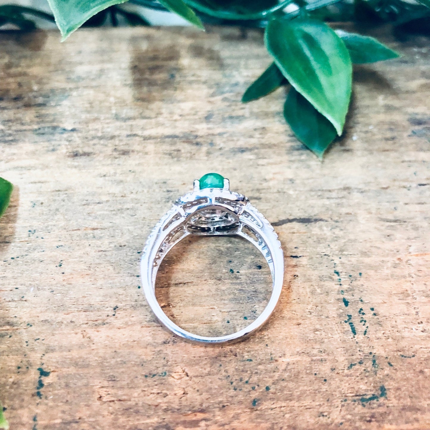 Vintage silver ring with green and opalescent stones on wooden surface surrounded by green leaves