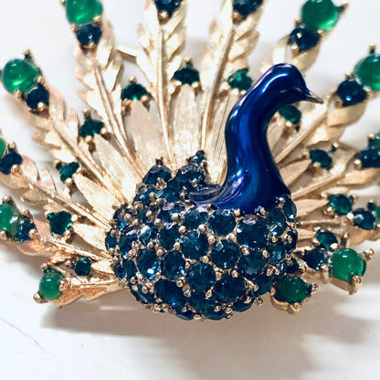 Alt text: Vintage gold-toned Boucher peacock brooch pin with blue gemstones and green beads forming the fanned tail feathers, creating an elegant and eye-catching piece of bird jewelry.