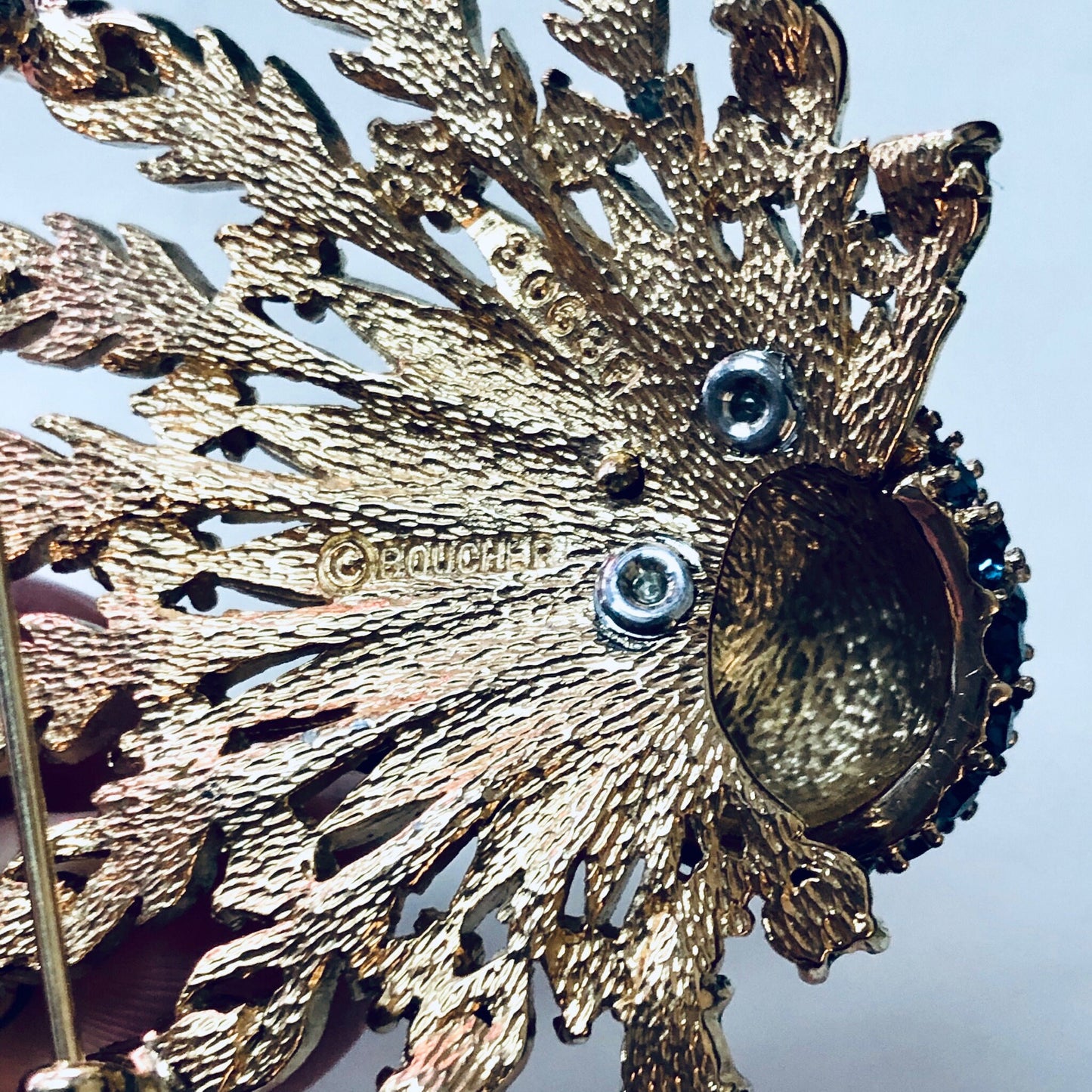 Vintage gold-toned Boucher peacock brooch pin with intricate feather details, blue gemstones for eyes, and green bead accents, capturing the majestic beauty of the bird in an elegant piece of statement jewelry.