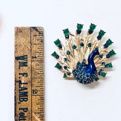 Vintage Boucher peacock brooch pin with blue gemstones, green beads, and gold tone in bird design, shown next to ruler for scale.