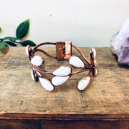 Vintage copper Matisse jewelry set with white enamel accents, including a hinged cuff bracelet and brooch, displayed on a wooden surface with crystal and greenery in the background.