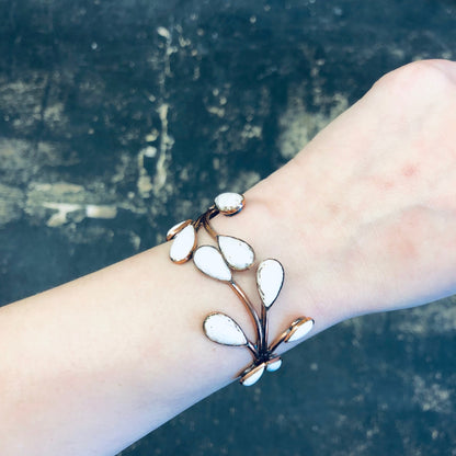 Vintage copper jewelry set with white enamel leaves worn on a wrist against a textured background