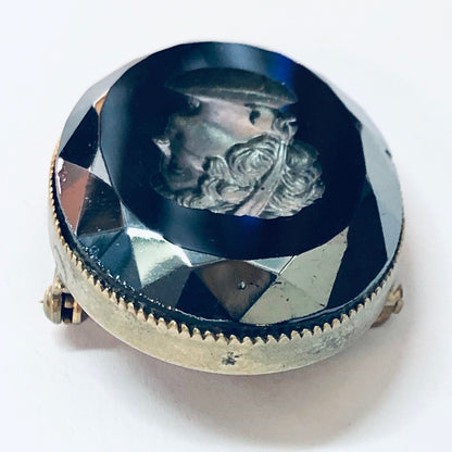 Vintage silver-toned brooch featuring a unique black cameo with an etched portrait design, set against a faceted dark blue background.