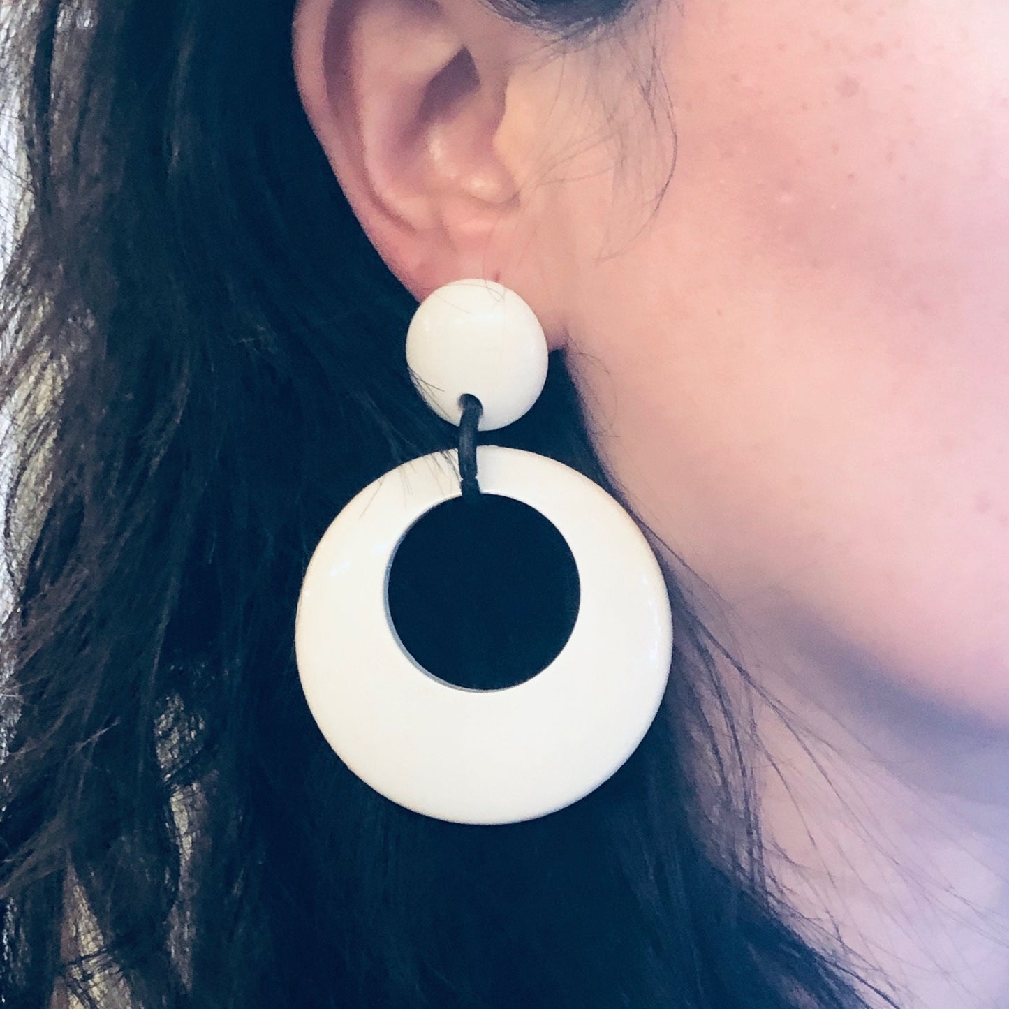 Woman wearing large black and white circular dangle earrings against her dark hair