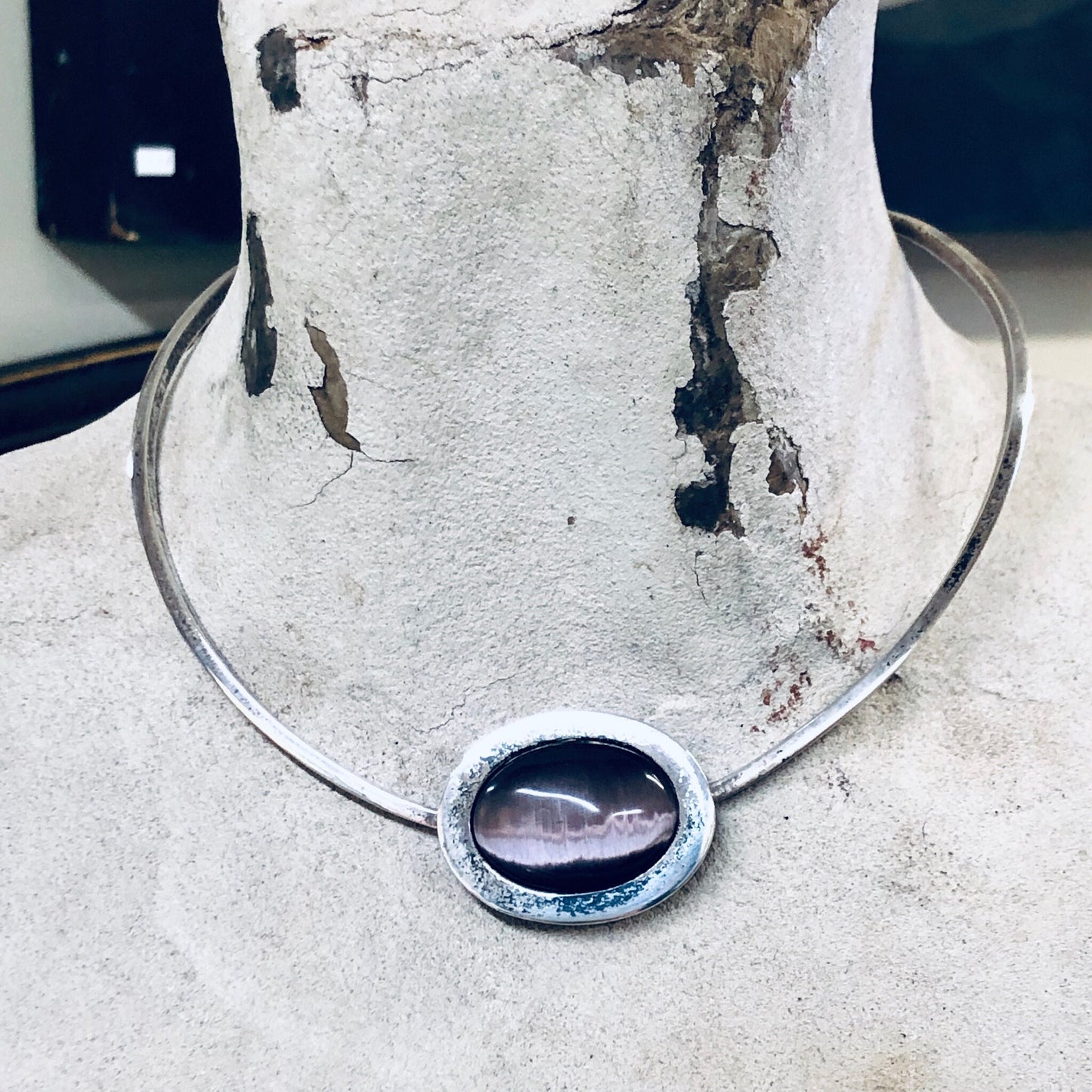 Silver choker necklace with purple tiger's eye gemstone on weathered concrete surface