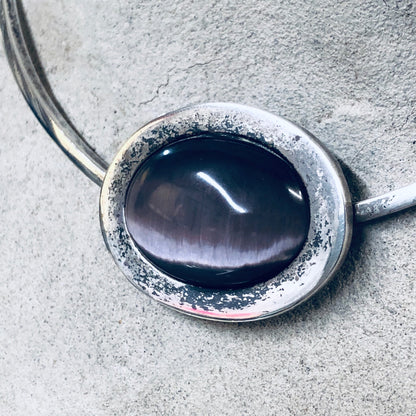 Vintage silver choker necklace with large oval purple tiger's eye gemstone on textured silver background