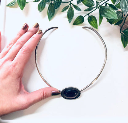 Vintage silver choker necklace with purple tiger's eye gemstone held in front of green leaves, showing a hand modeling the necklace against a white background.