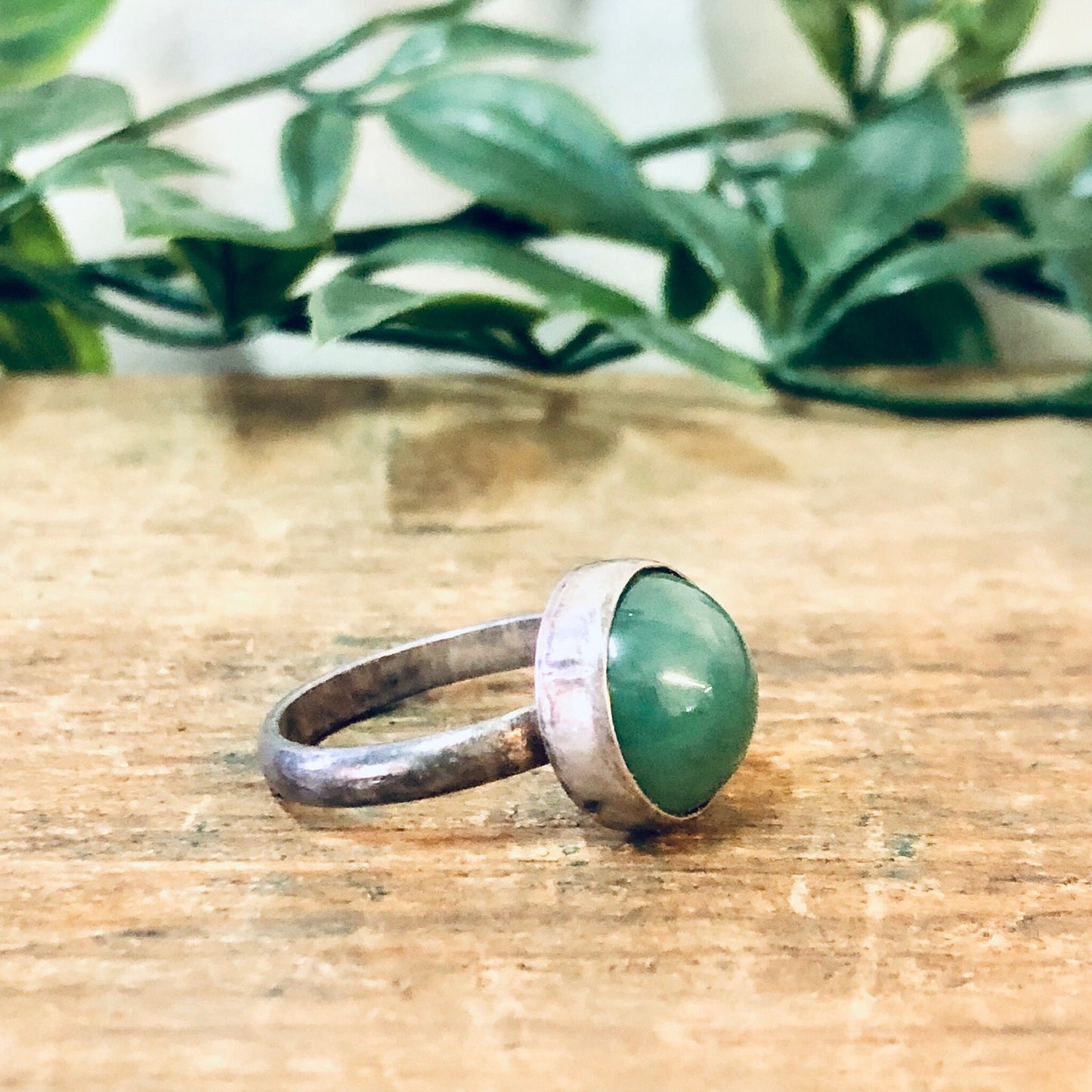 Vintage silver ring with round green gemstone cabochon on rustic wooden surface with greenery in background