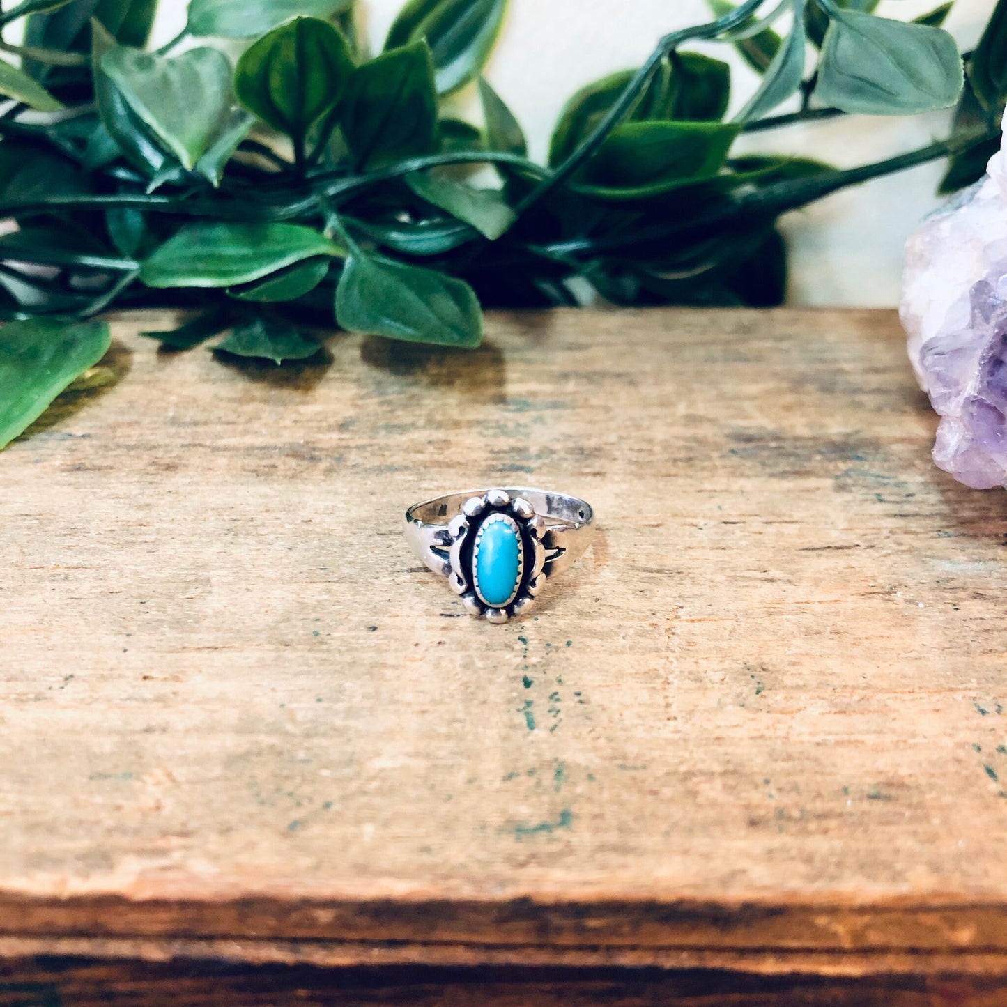 Vintage silver and turquoise ring displayed on rustic wooden surface next to green foliage