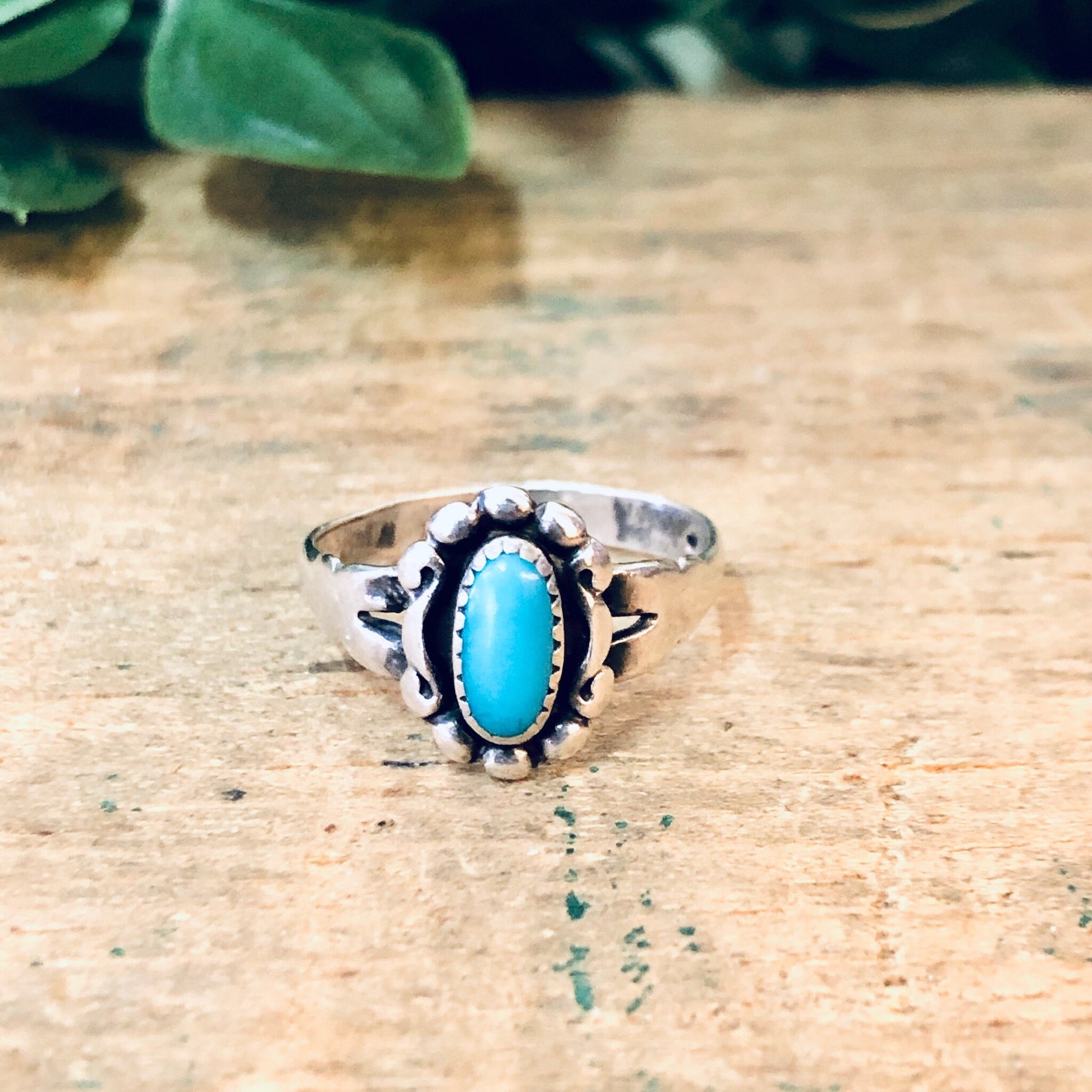 Vintage silver turquoise ring with ornate setting on wooden surface with greenery in background