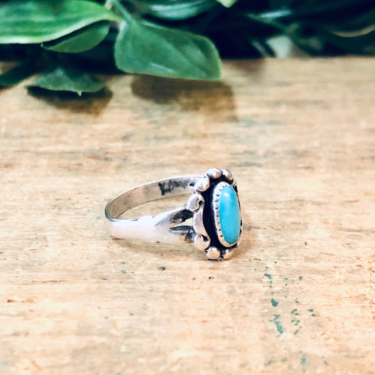 Vintage silver turquoise pinky ring on wooden surface with green foliage in background