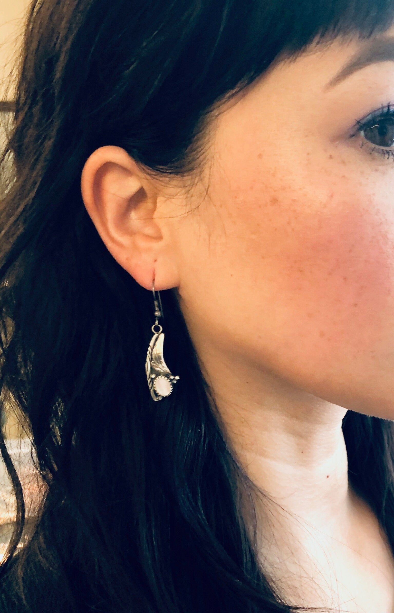 Close-up of a woman wearing vintage silver dangle earrings with mother of pearl accents, against her dark hair