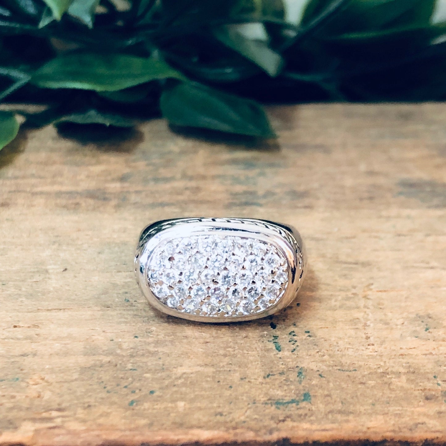 Vintage silver ring with sparkling faux diamonds and intricate rope design, placed on rustic wooden surface with green foliage in the background