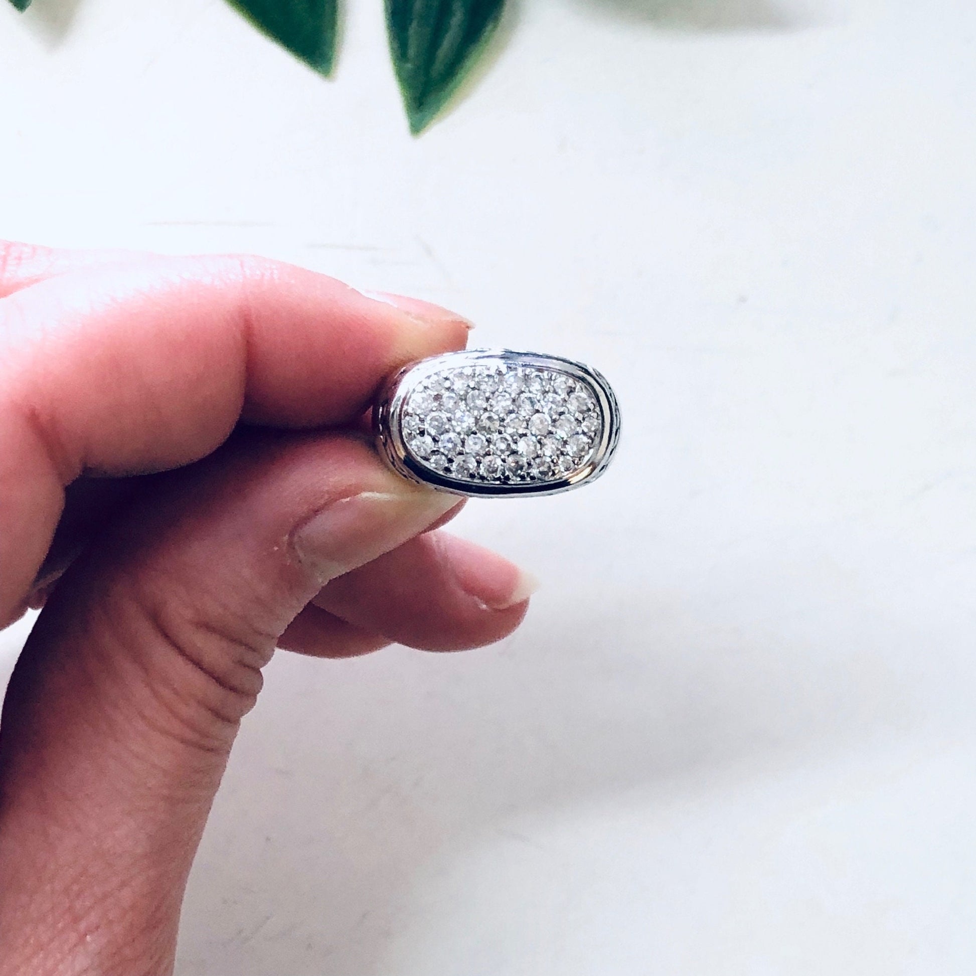 Vintage silver rope design ring with sparkling faux diamond centerpiece, held between fingers over white background with green leaves