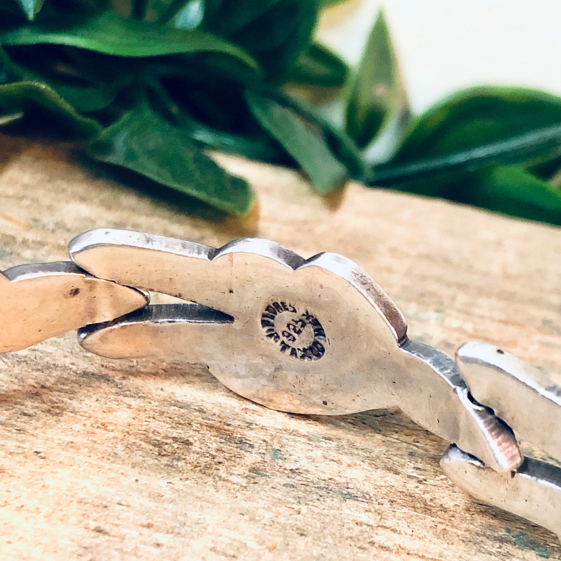 Vintage Taxco silver link bracelet by J. Flores featuring a modernist design with a round centerpiece detail, displayed on a rustic wooden surface with green foliage in the background.