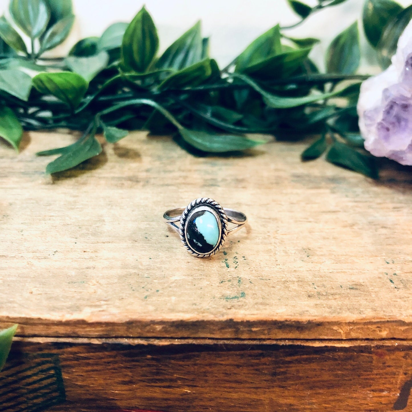 Vintage silver ring with oval blue cabochon stone surrounded by green leaves on a wooden surface