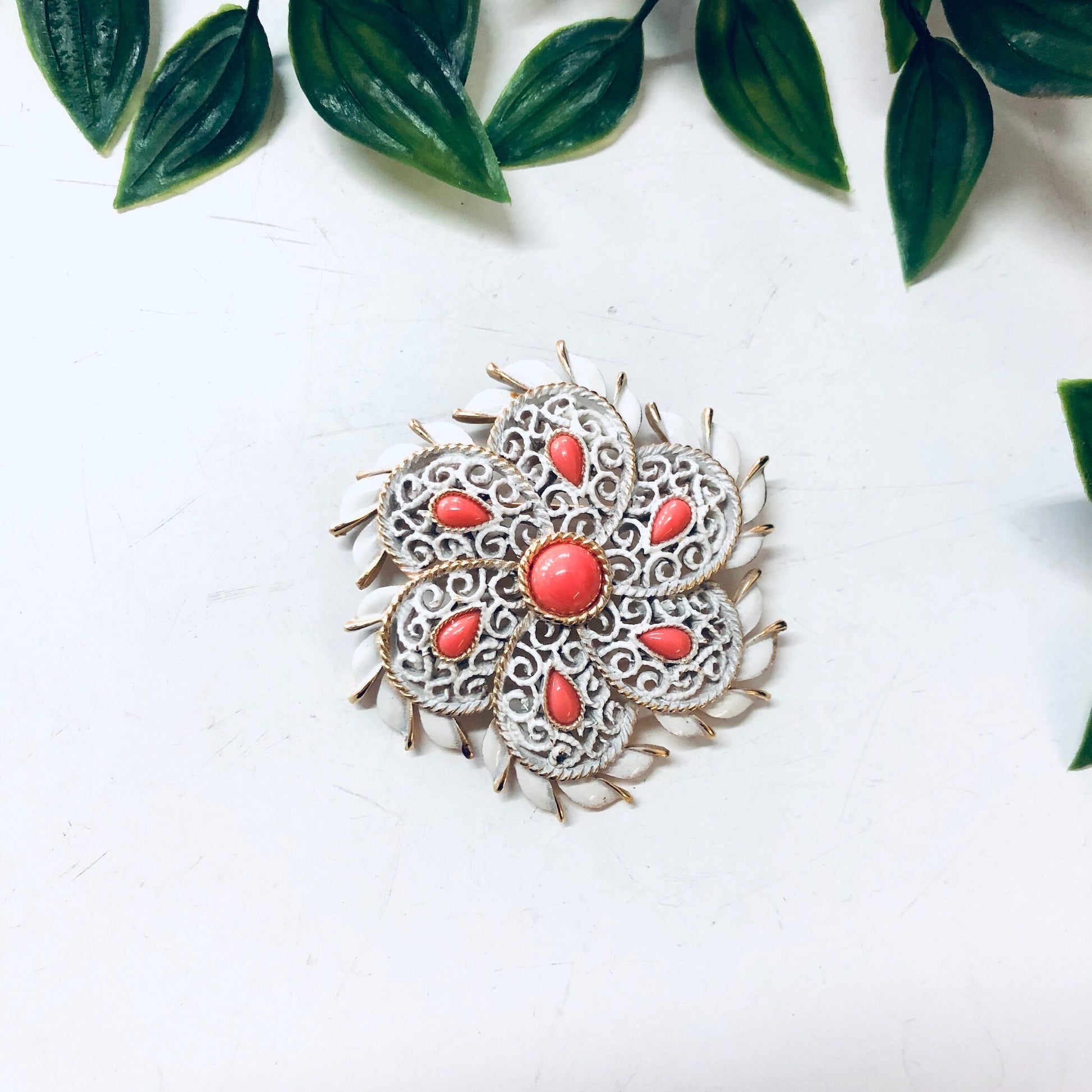 Vintage Trifari brooch with orange cabochons and gold-toned accents, surrounded by green leaves on a white background.