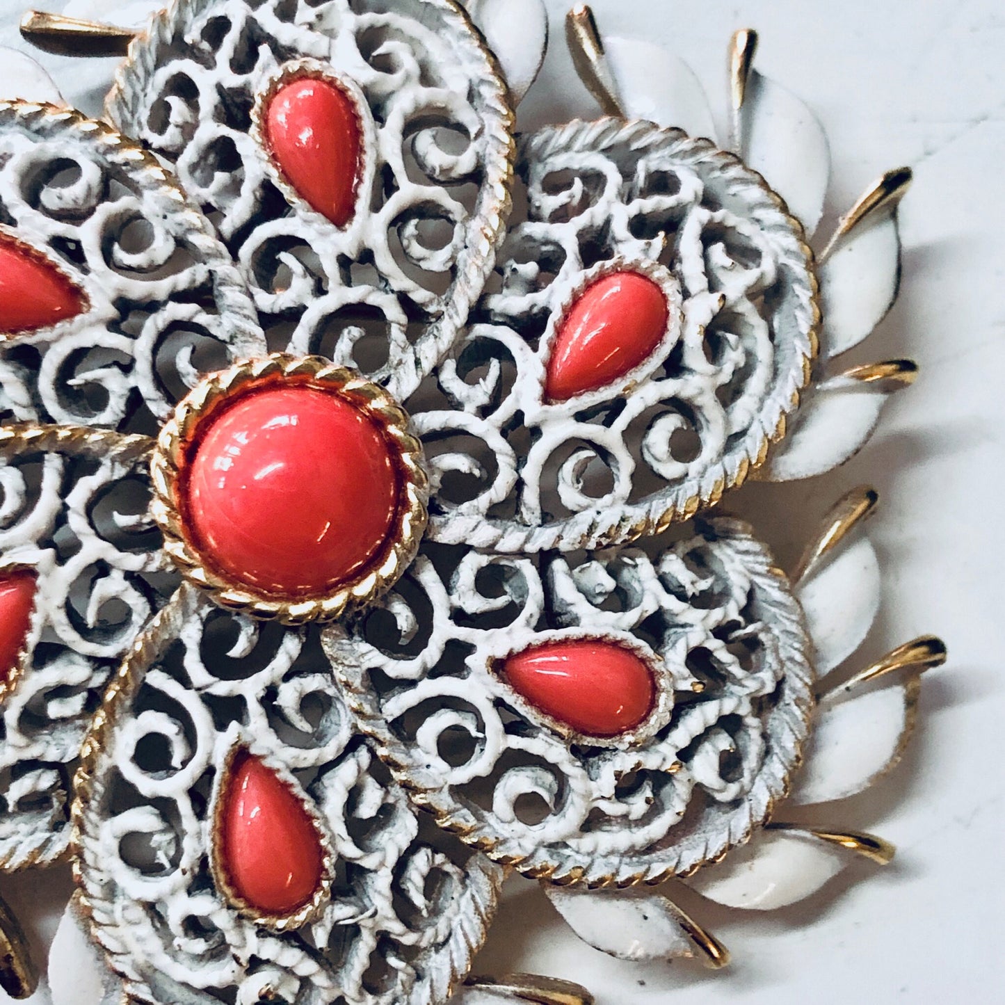 Vintage Trifari brooch with white enamel filigree design, orange cabochon accents, and gold-tone metal detailing, creating a bold statement jewelry piece from a renowned vintage brand.