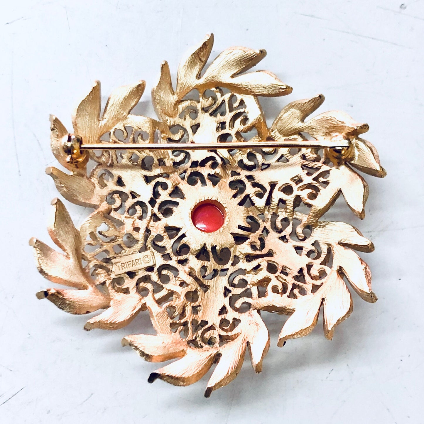 Vintage gold-tone Trifari brooch with intricate cutout leaf design, white enamel base, and central orange cabochon accent, creating a bold statement jewelry piece from a renowned vintage brand.